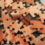 A close-up view of scattered wooden jigsaw puzzle pieces on a dark surface.