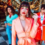 Stylish individuals in brightly colored outfits posing fashionably indoors with bokeh lights.