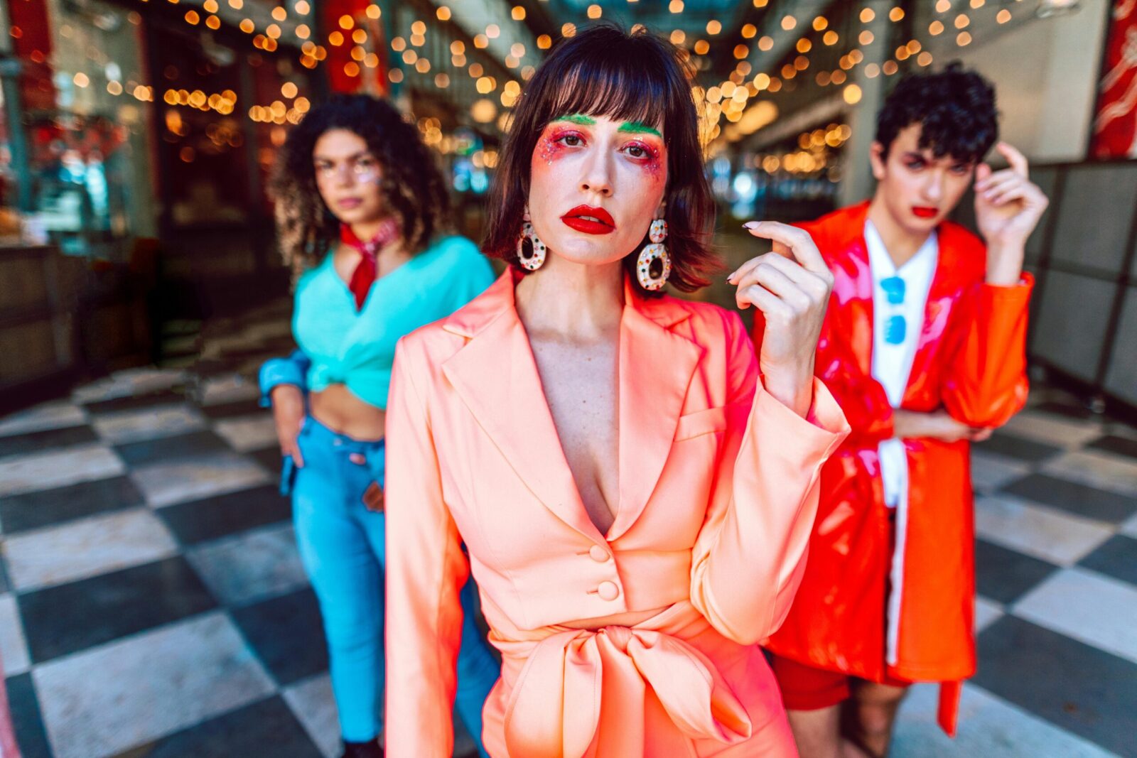 Stylish individuals in brightly colored outfits posing fashionably indoors with bokeh lights.