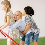 Three children joyfully play indoors with a hula hoop, showcasing happiness and togetherness.